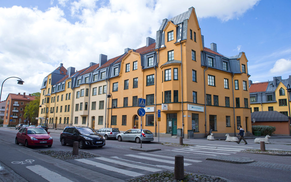 En bilväg med övergångsställe intill flerbostadshus i ljusa färger, foto.