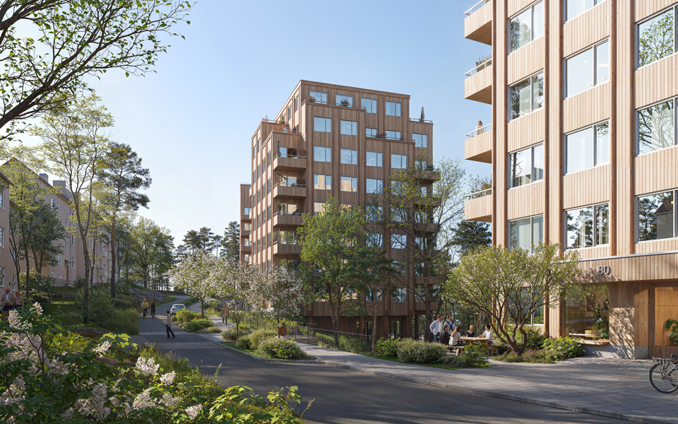 Visionsbild över förslaget sett från den nya gatan. Bilden visar framförallt de två byggnaderna i mitten av förslaget, det västligaste huset skymtas i bakgrunden. Husen är punkthus i trä med indragna balkonger. På de lägre våningsplanen är balkongerna placerade i hörnen. De två översta våningarna har indragna balkonger på husets sidor vilket gör att volymen trappas av uppåt. Den nya gatan visas centralt i bilden. En gångbana går längs gatans högra sida, framför den nya bebyggelsen. På en del av gatan, mellan körbanan och gångbanan finns en planteringsyta. Bakom planteringsytan skymtas en bil, vilket visar att det finns plats för parkering där. Vid planteringsytan, mellan de två byggnaderna, syns räcken och en avsatts i trä vilket är början den föreslagna kopplingen mellan befintligt gångstråk från Gröndalsvägen och den nya gatan. Där finns även en upphöjd övergång över gatan.  