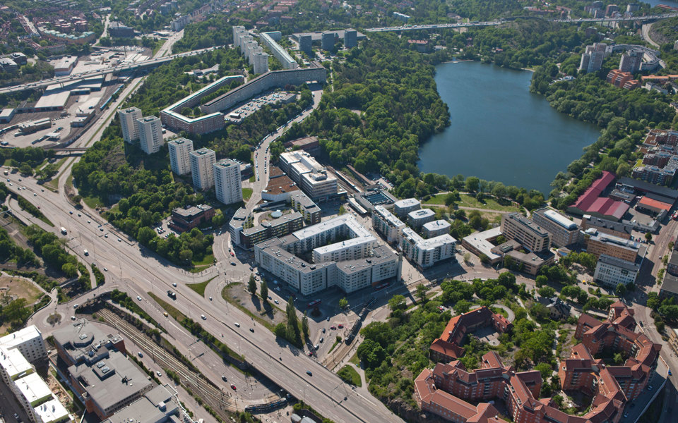 Flygvy över Liljeholmen. Vägar med fordon i rörelse. Bostadsområden, områden för verksamheter och grönområden. En sjö. Foto.