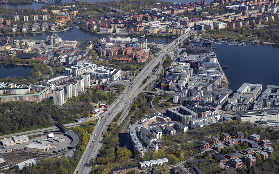Flygvy över Liljeholmen med bostadshus och grönska, omgivet av vatten, foto.