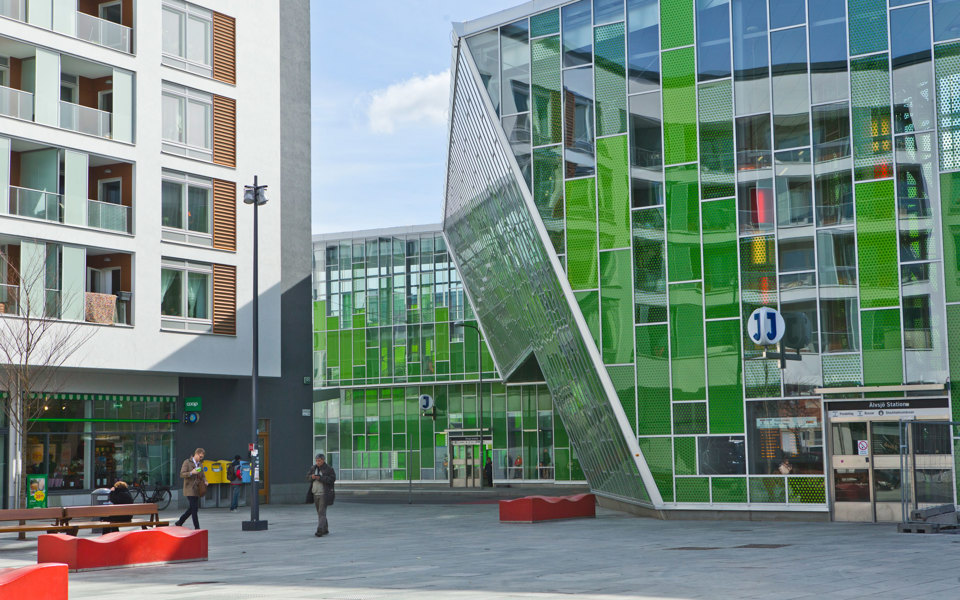 Moderna grön- och silverfärgade hus intill torg vid järnvägsstation, foto.