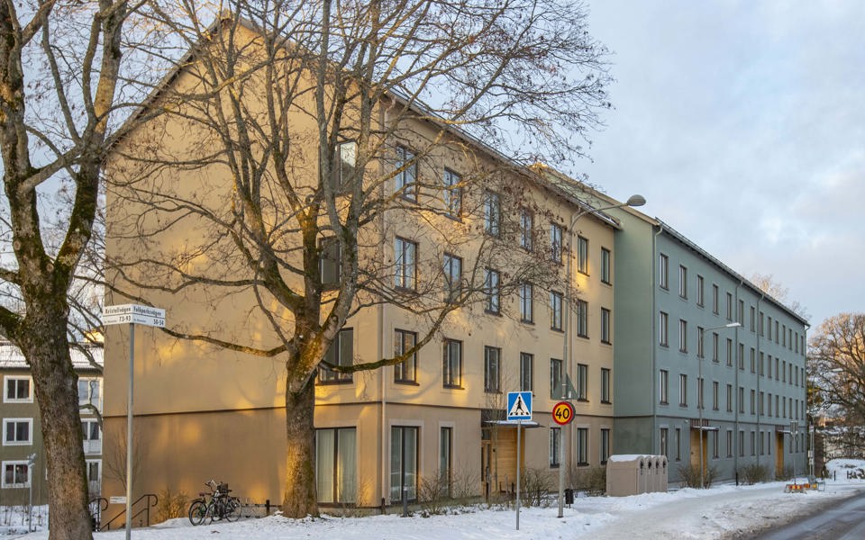 Vy mot lamellhus på fyra våningar längs en gata, foto. 