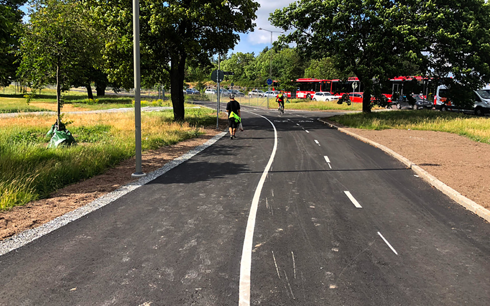 En person som går och en person som cyklar på Hässelbystråket. Gräs och träd vid sidan om stråket. Foto.