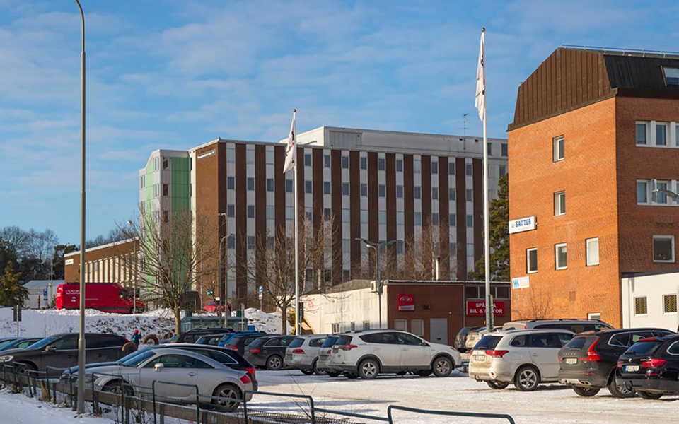 Kontorshus med bilparkering utanför. Flera parkerade bilar. Foto.