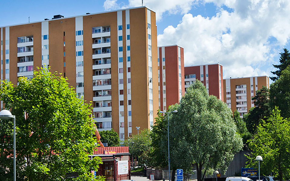 Bostadshus med flera våningar. Omgivande träd. Foto.
