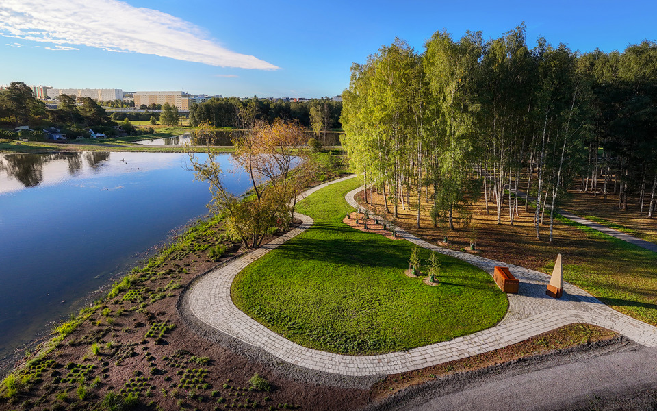 Vy över urngravområde men vatten bredvid. Hus längre bort speglas i vattnet.