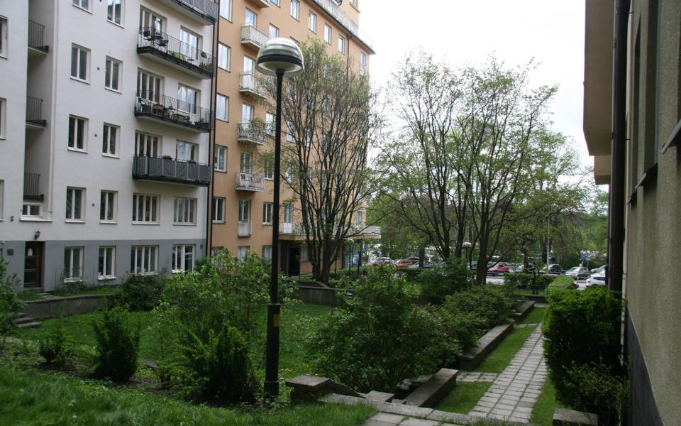 En liten park omgiven av flerbostadshus med stenbelagda gångar. Foto.