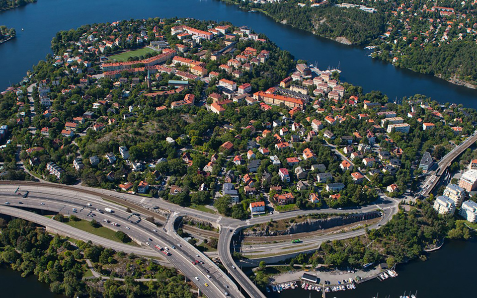 Ö med hus, skog, bilvägar och bro. Foto.