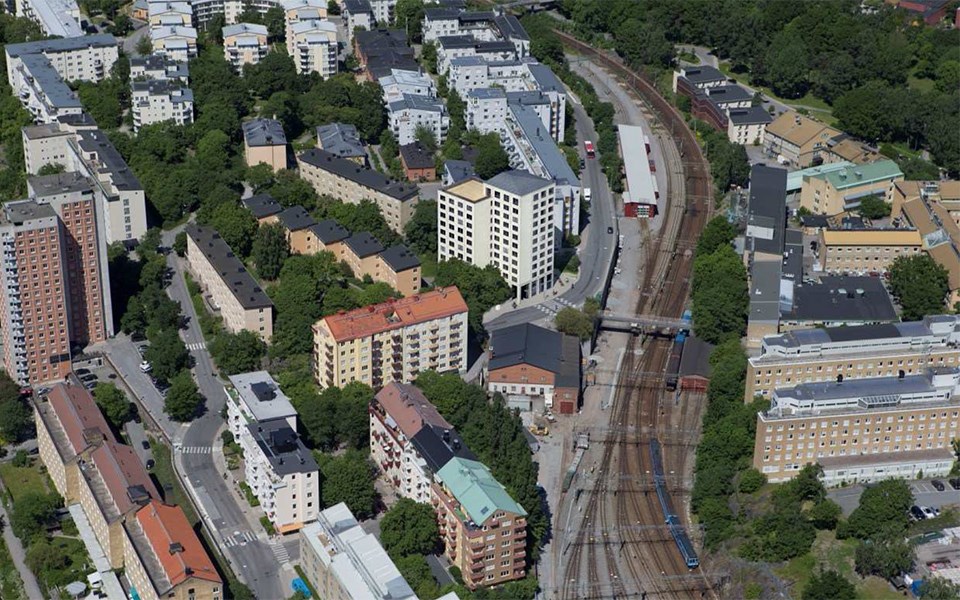 Flygfotografi över ett område med flerbostadshus och järnvägsspår.