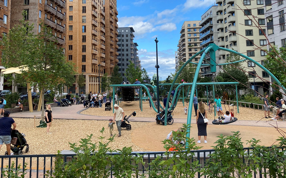 Lekplats i Norra Stationsparken omgiven av flerfamiljehus med barn och vuxna som leker och promenerar. 