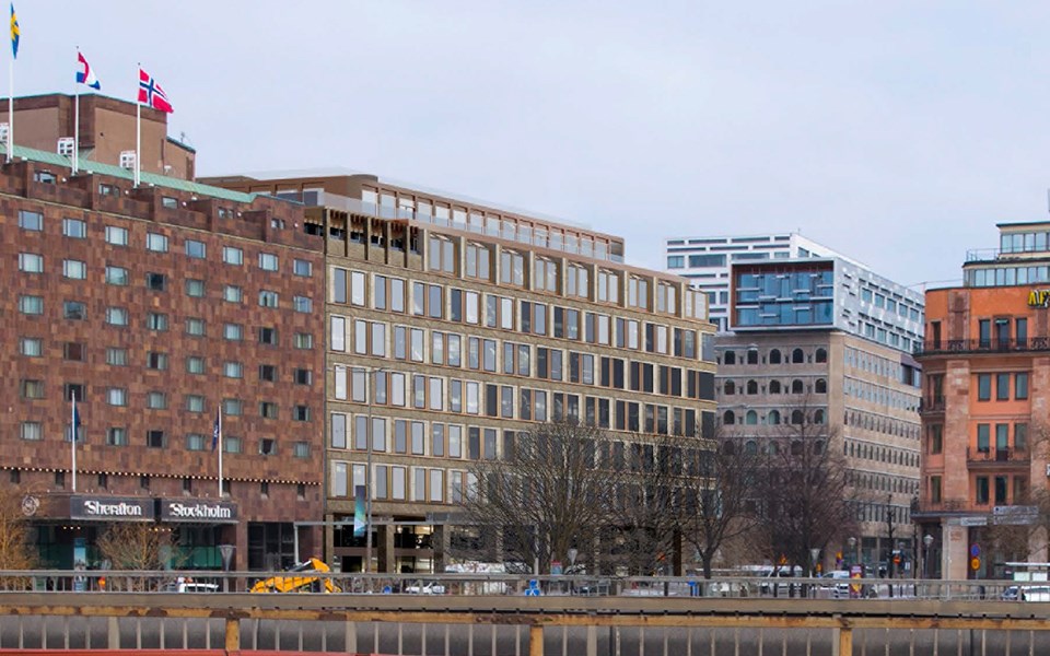 Fasaderna till fyra stora kontorsbyggnader i grått och tegelfärg. Ett av husen har svenska, franska och norska flaggan på taket. Framför husen syns en trafikerad väg.