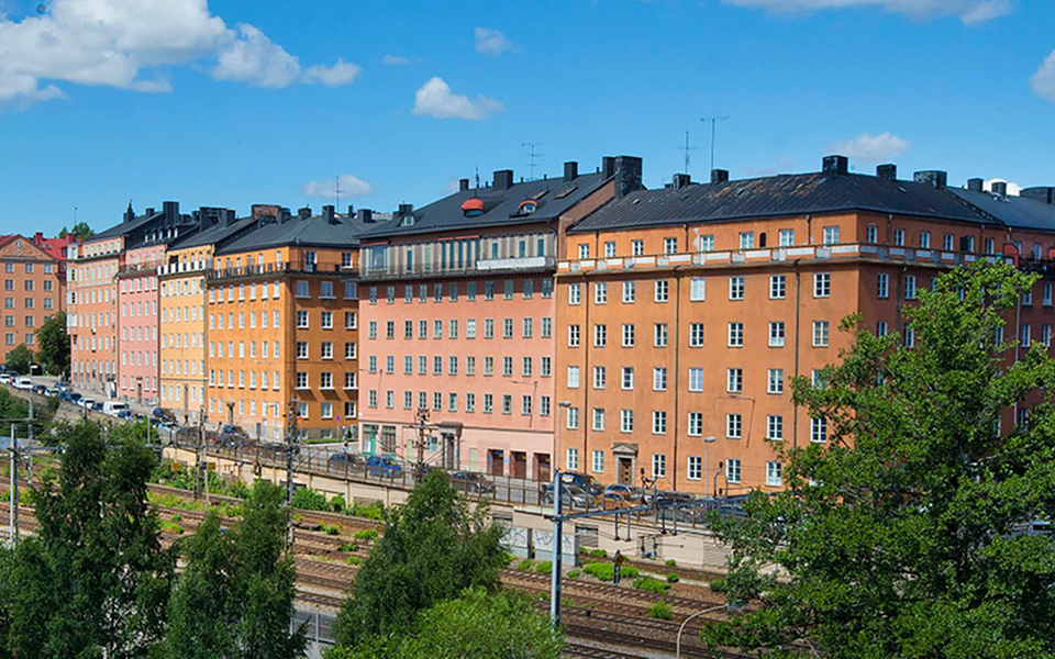 Bostadshus i flera olika färger. Omgivande träd, tågspår och gator med bilar. Foto.