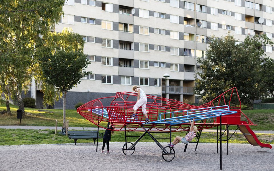 Klätterställning i form av ett flygplan i park vid bostadshus och träd. Barn som klättrar, foto.