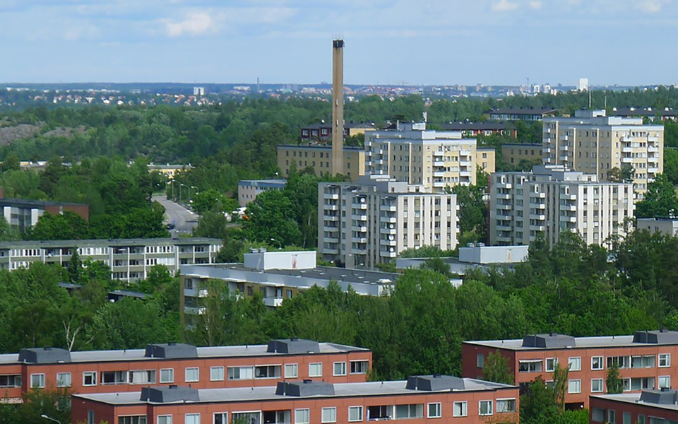 Höga bostadshus med flera våningar och balkonger med omgivande träd och berg. Foto.