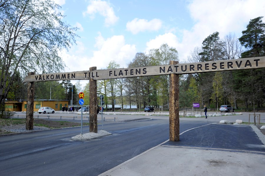 Infart till parkering vid naturreservat. Skylt i trä ovanför infarten  där det står "Välkommen till Flatens naturreservat".