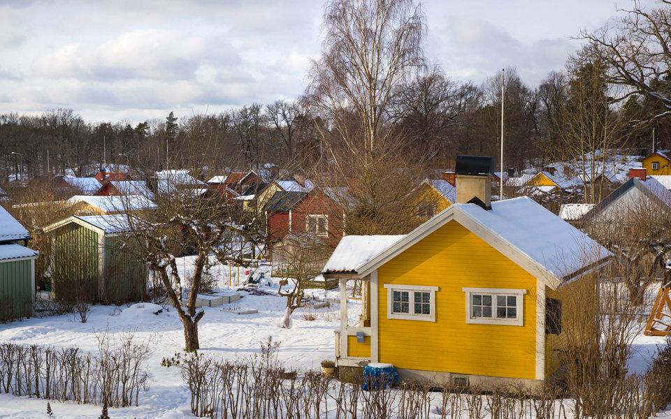 Små färgglada stugor med trädgårdar. Snö på marken, foto.