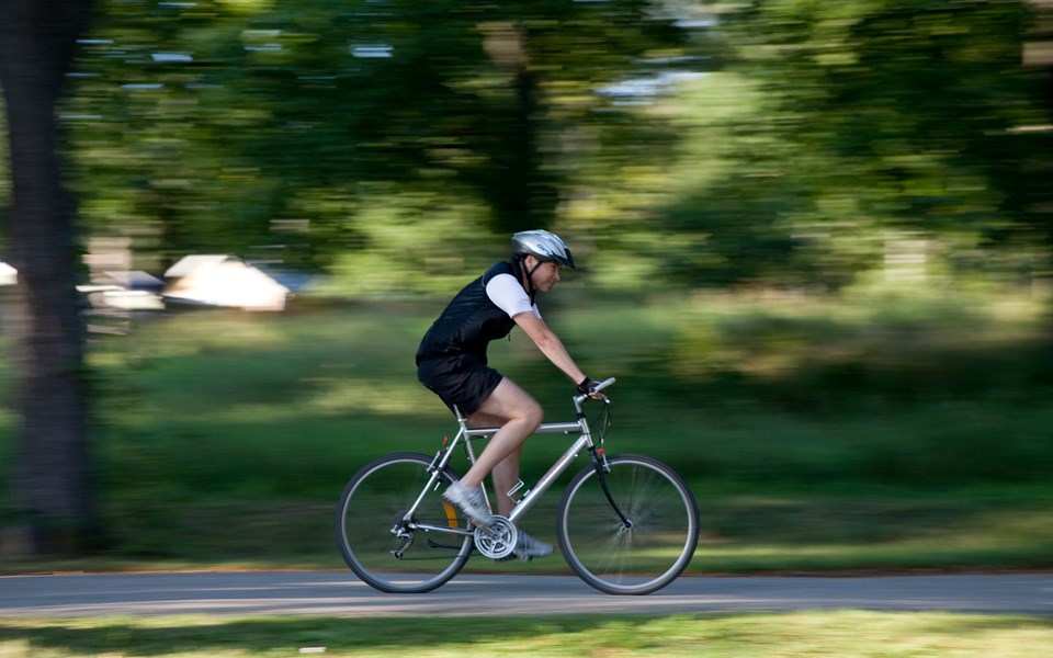 En cyklist som cyklar på en väg genom grönområde, sett från sidan, foto.