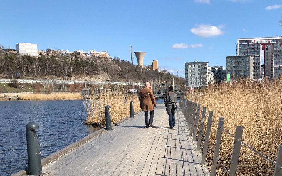 Två personer syns bakifrån, gåendes på en strandpromenad, fotografi.