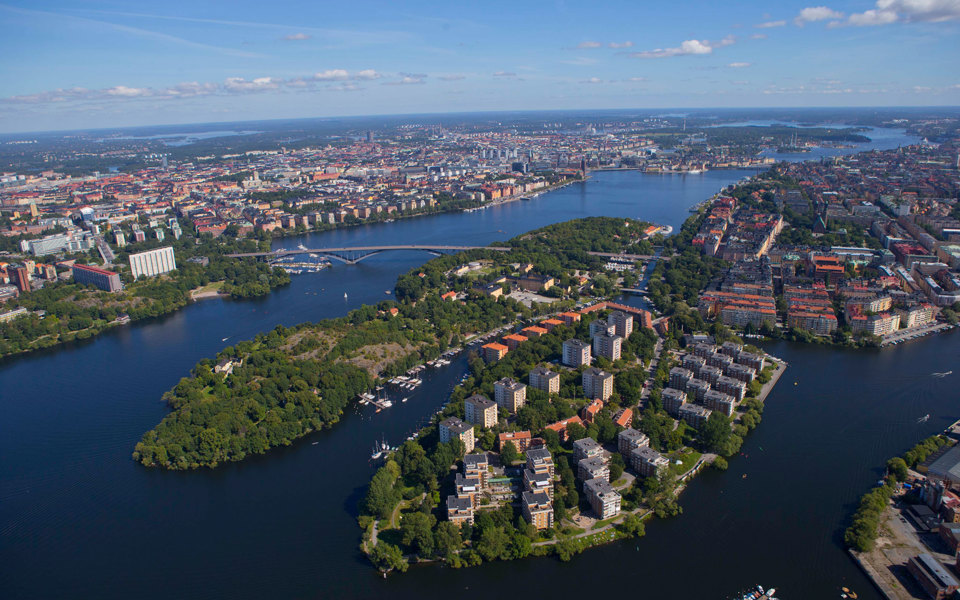Flygfoto över område med hus, grönområden och vatten. 