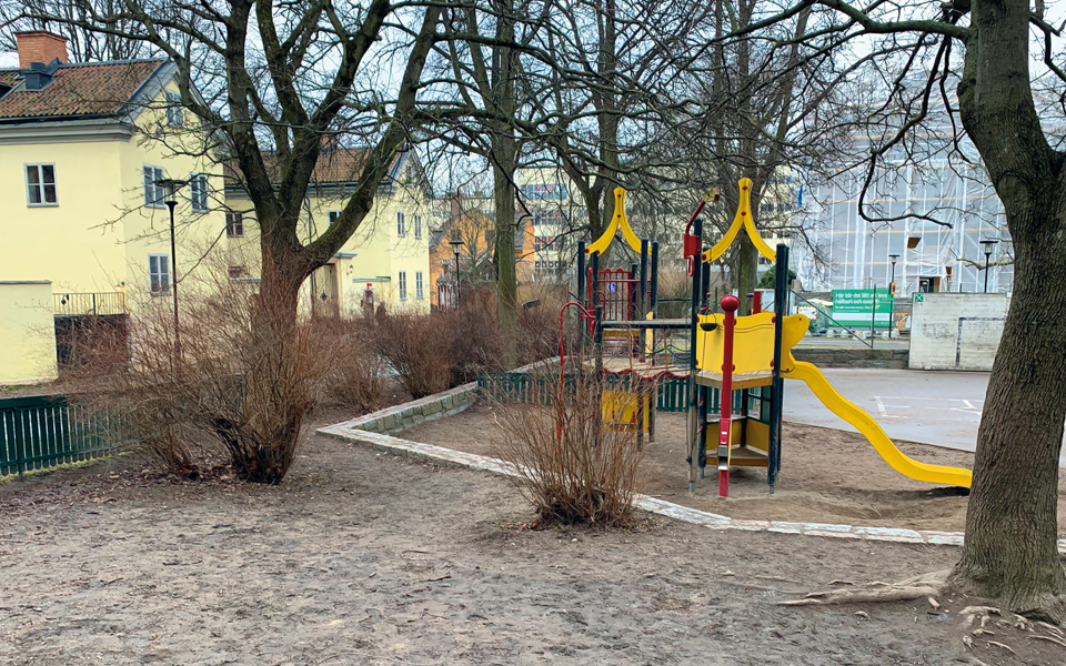 Lekplats med sandlåda med omgivande flerbostadshus och träd, fotografi.