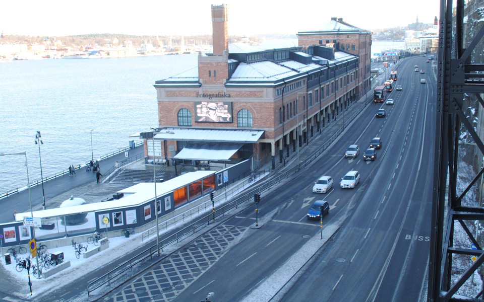 Fotografiska muséet, bilväg med bilar och buss som kör, vatten och människor i rörelse. Foto.
