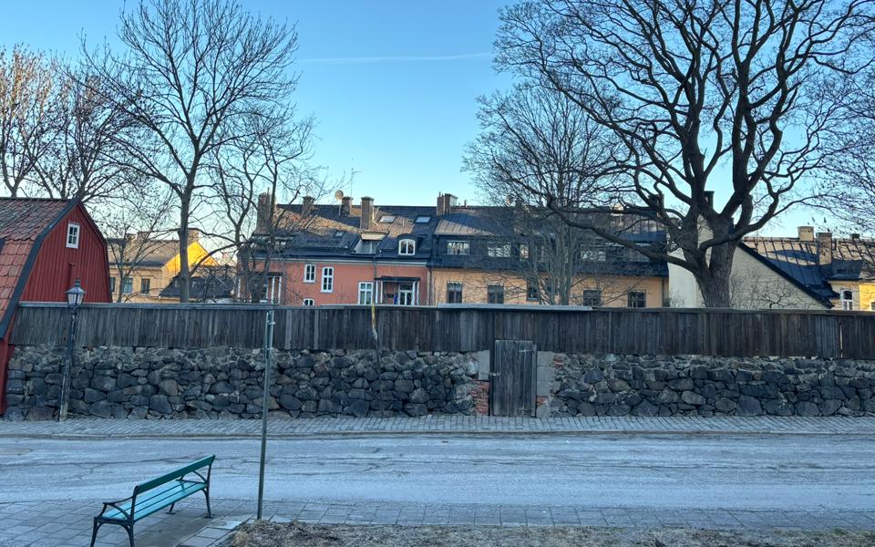 En gammal stenmur i svarta stenar längs Stigbergsgatan i Stockholm. Bilden visar murens struktur och omgivande fastigheter.