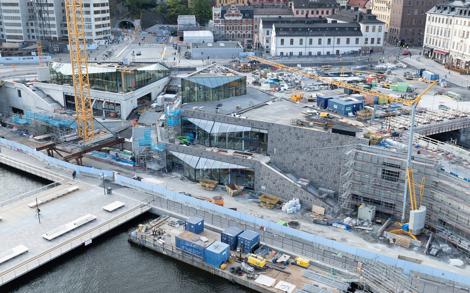 Byggarbetsplatsen vid Slussen. Vy ovanifrån över byggnation av Mälarterrassen med glaspaviljonger och fasader av granit. I bakgrunden ligger Ryssgården och Katarinahuset.