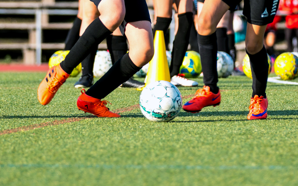 Fotbollsspelare som sparkar på en boll på ett underlag av konstgräs.