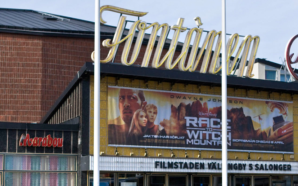 Biografen Fontänen sett från torget. På taket finns ljusskyltar och över ingången hänger reklam för en film som visas.