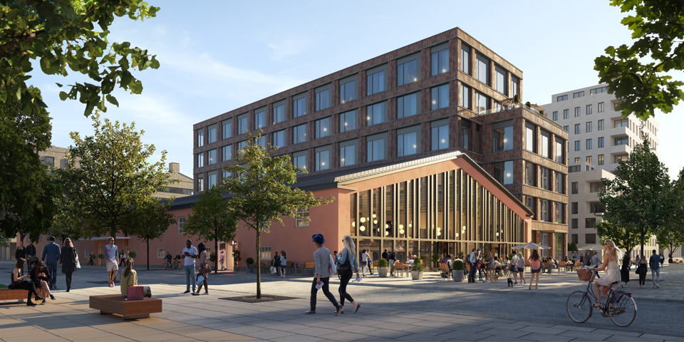 En modern byggnad med stora glasfönster bredvid en renoverad industribyggnad i en stadsmiljö. Människor promenerar, cyklar och sitter på bänkar i ett grönskande torgområde framför byggnaden.