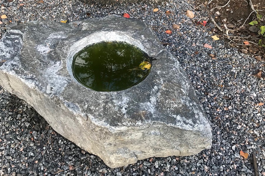 En sten på marken med ett runt hål fyllt med vatten.